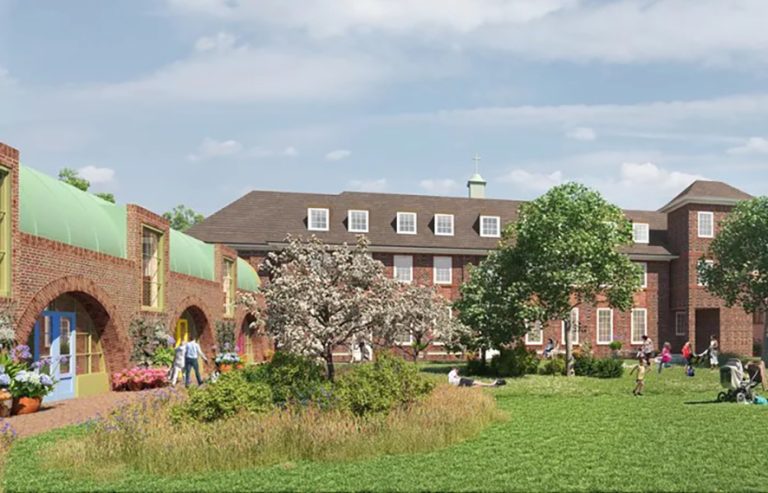 People sitting and playing in a grassy area surrounding by buildings on a sunny day.
