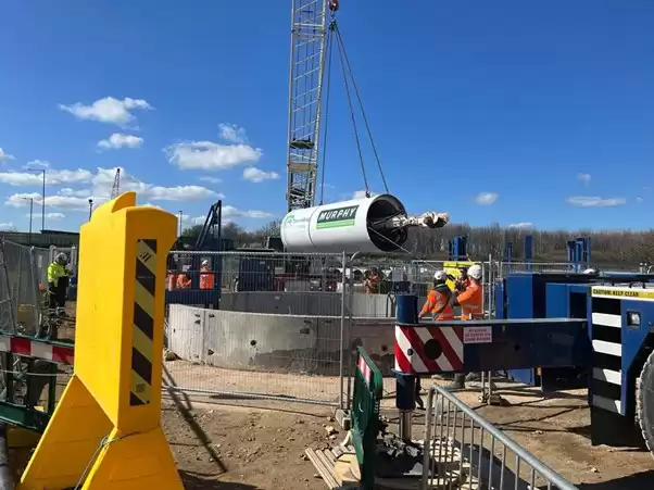 A crane lowering Murphy-branded tunnelling equipment into a concrete cylinder at a onshore cable civils works.