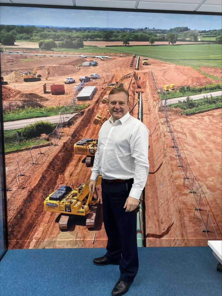 A portrait image of the Energy Director, stood before a graphic of machinery on-site.