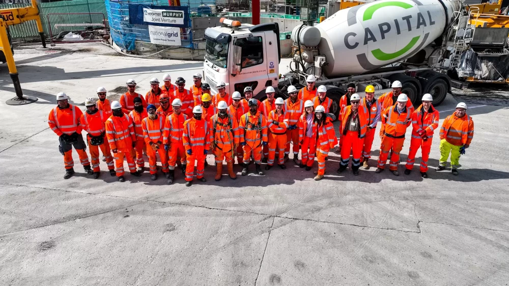 A group of people in safety uniform and helmets stood in front of a concreate mixer with the word 'capital' on the side.
