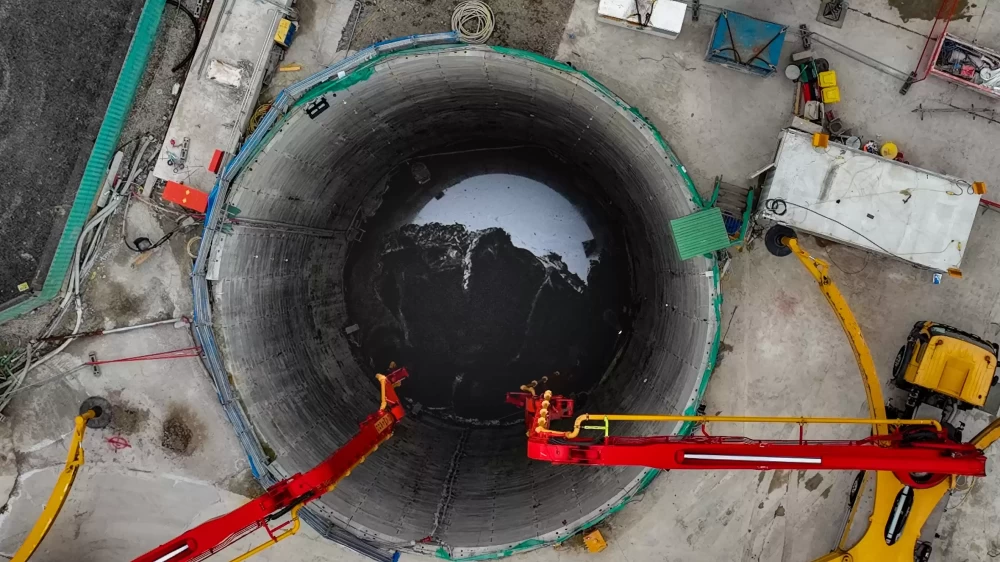An aerial view of a power tunnel construction site with red and yellow construction vehicles.