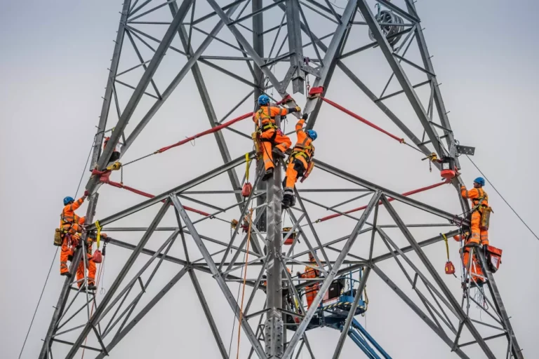 People wearing helmets and orange safety uniform working on an electricity pylon.