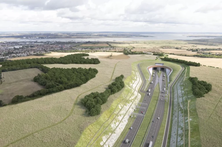 An aerial view of a road leading into a tunnel surrounded by fields with houses in the distance.