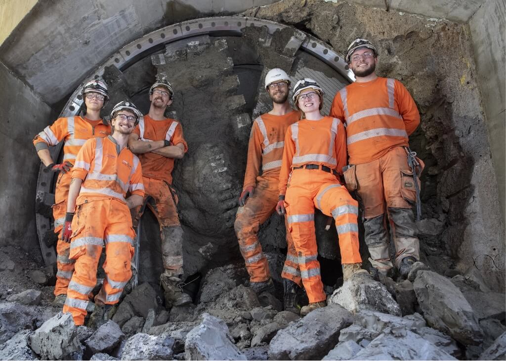 A group of workers in Murphy branded uniform and safety helmets standing in a tunnel in front of some machinery.
