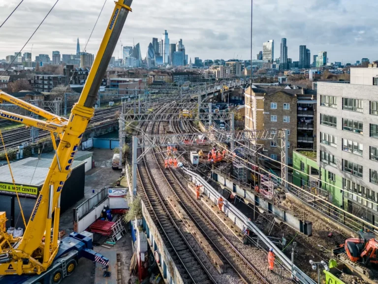 An aerial view of railway tracks under construction with a cityscape in the background.