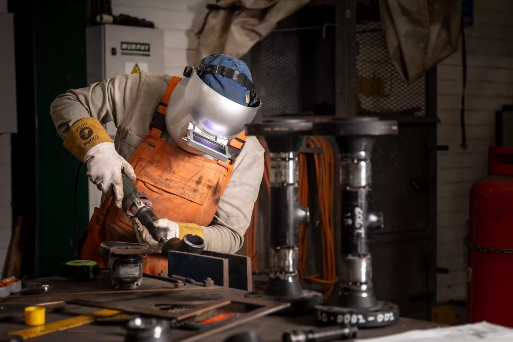 A person wearing a silver safety mask welding a piece of metal.