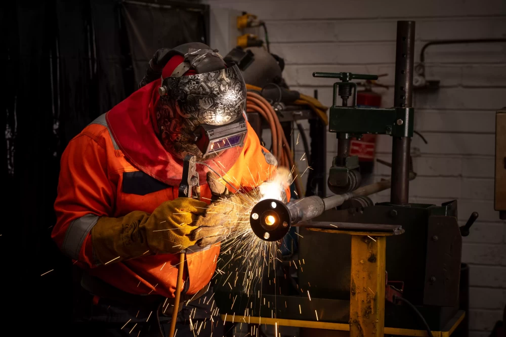 A person wearing a safety mask and gloves welding a piece of metal.
