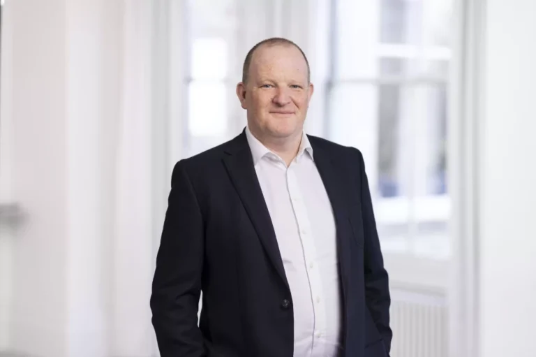 A man in business dress posing for a photo in a white room.