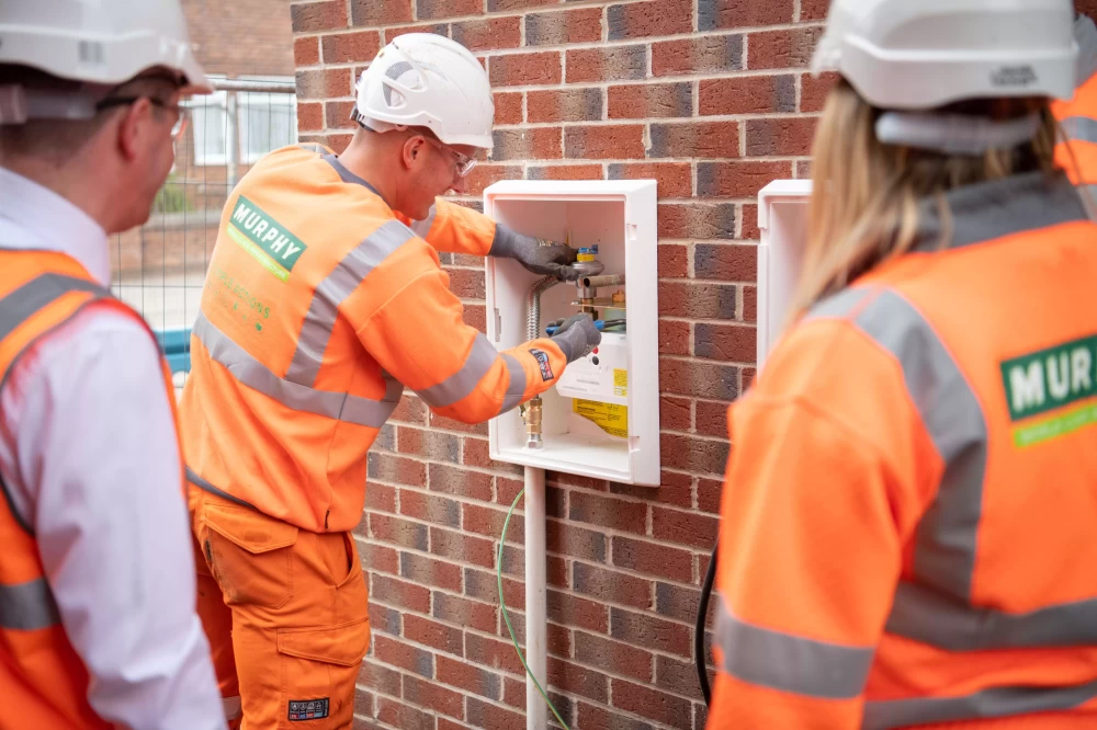 A Murphy employee working on a meter on the side of house with other Murphy employees in the background watching.