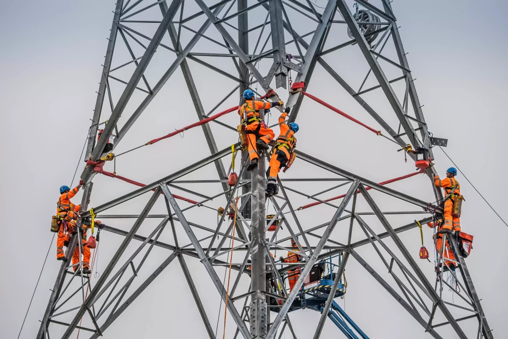 People wearing helmets and orange safety uniform working on an electricity pylon.