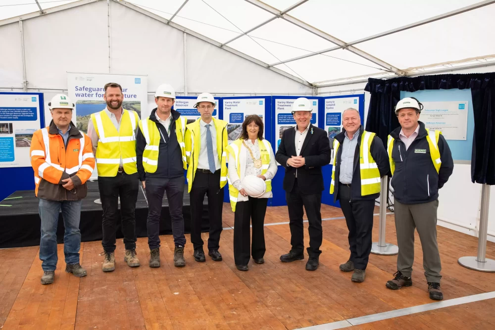 A group of people in high-visibility jackets smiling in front of a small stage.