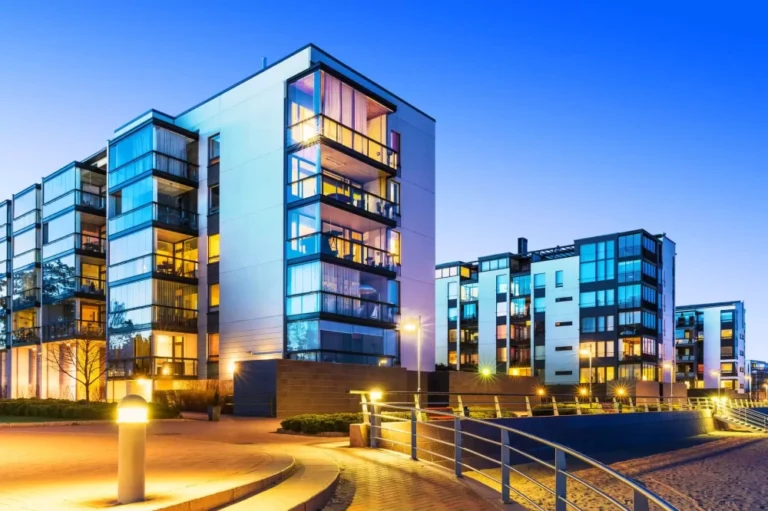 Apartment blocks with a pavement lit up with street light and stairs leading down to a beach.