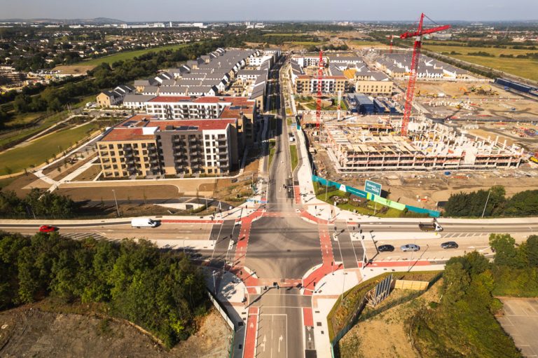 An aerial view of an intersection surrounded by construction, houses and fields.