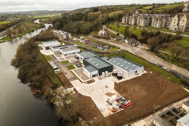 An aerial view of buildings at a water treatment plant with a river on one side and hills in the background.