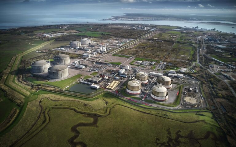 An aerial view of a Liquefied Natural Gas terminal surrounded by fields with a shoreline in the background.