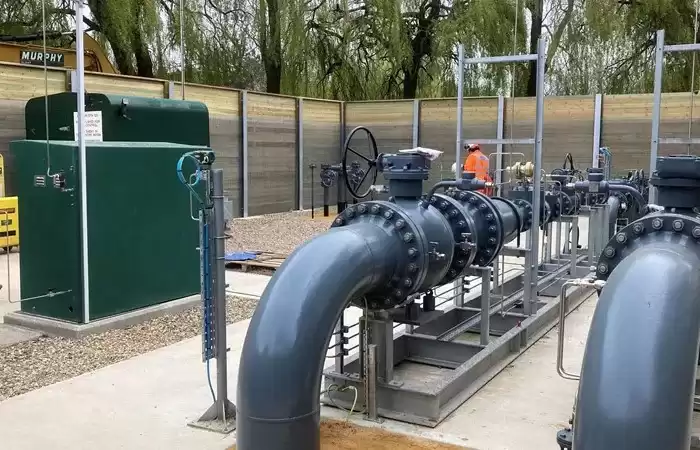 Gas transmission pipes surrounded by a wooden fence with trees in the background.