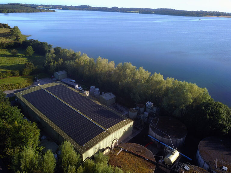 An aerial view of a water treatment works next to a large body of water surrounded by trees.