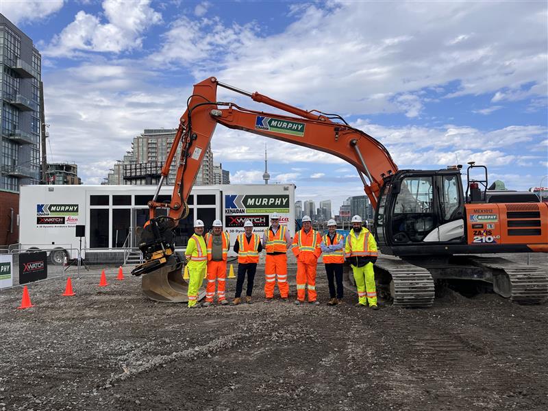 A group of people wearing safety equipment in front of a Murphy construction vehicle in Canada.