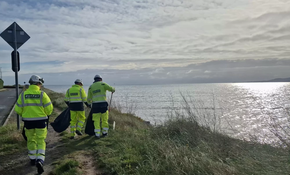 Three Murphy employees in high-visibility uniform and white helmets clearing litter next to a large body of water.