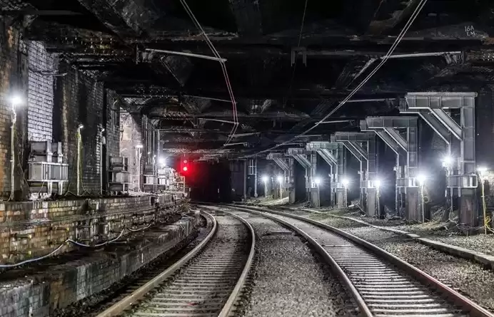 Brightly-lit underground train tracks leading into a tunnel.