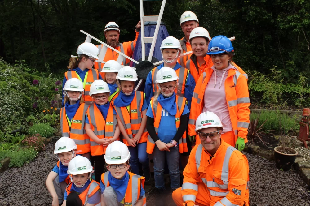 A group of children and Murphy employees wearing Murphy branded uniform and helmets stood in a garden.