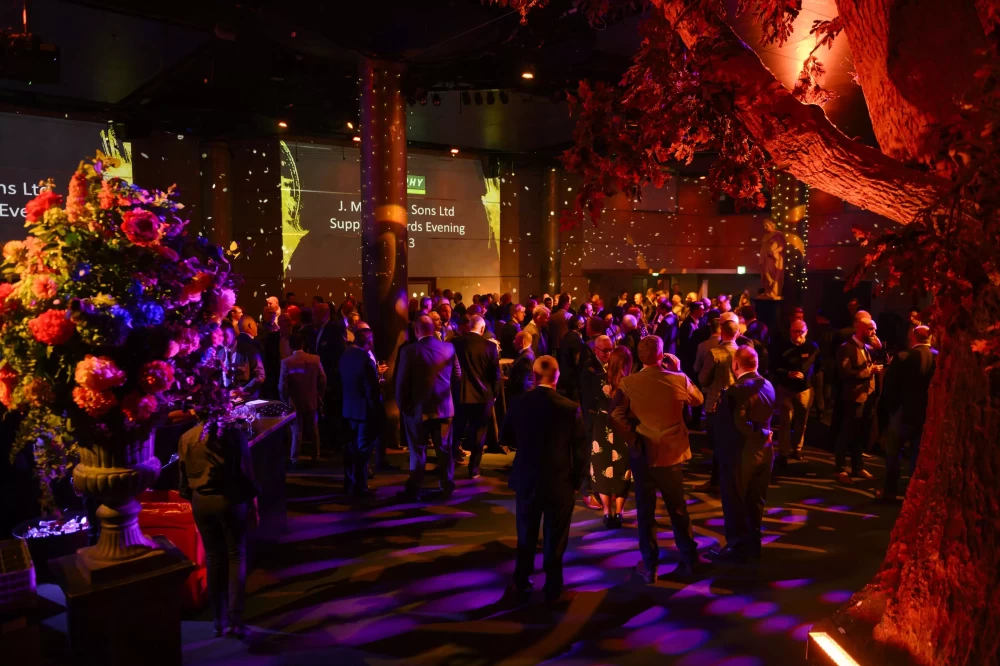 A group of people at an awards ceremony in a dimly lit room decorated with flowers, trees and lights.