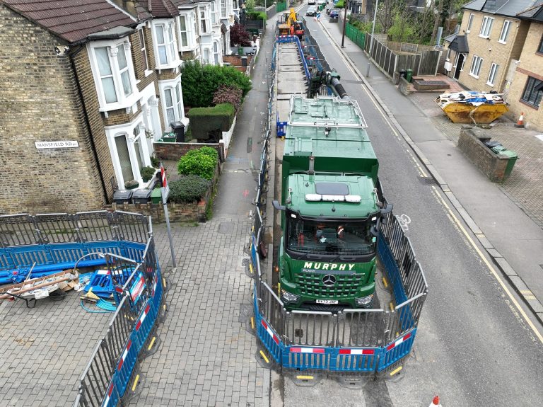 Water mains construction on a residential road with blue barriers marking the site and a green Murphy construction vehicle.