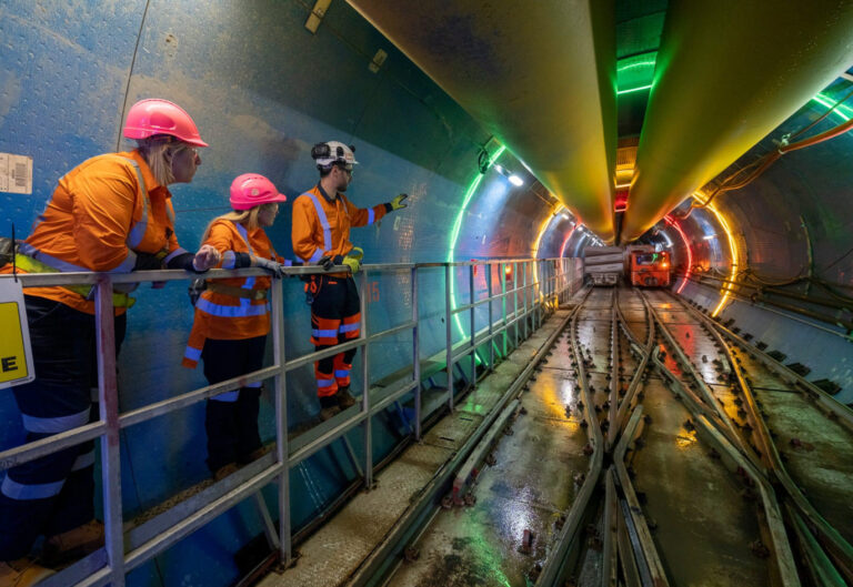 Three people in safety uniform inside an underground tunnel with tracks.