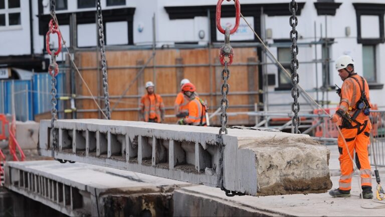 A large piece of concrete being lifted by chains on construction site with Murphy employees wearing safety equipment.