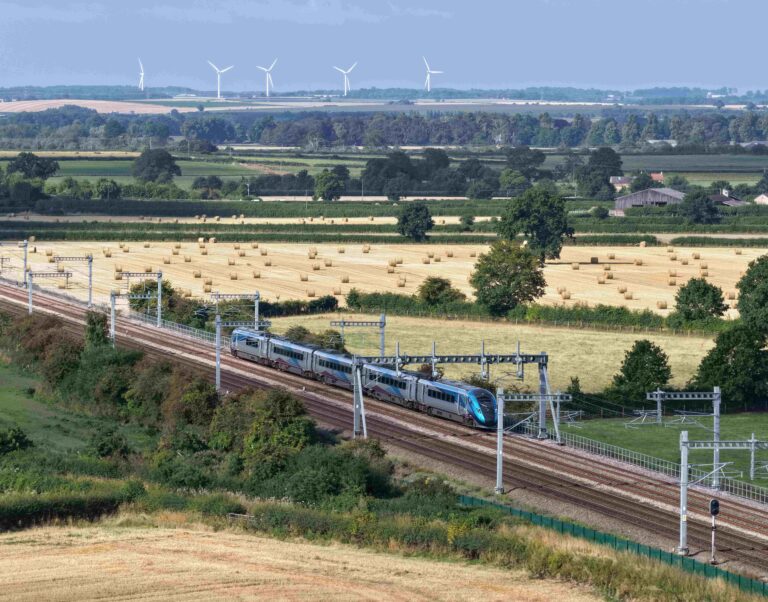 A large landscape with buildings, fields, trees, wind turbines and a blue and silver train.