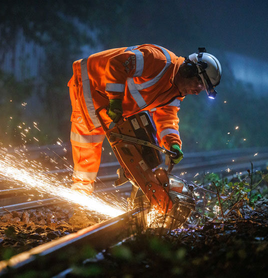 A Murphy employee in orange high-visibility uniform and a white helmet operating machinery on a train track.