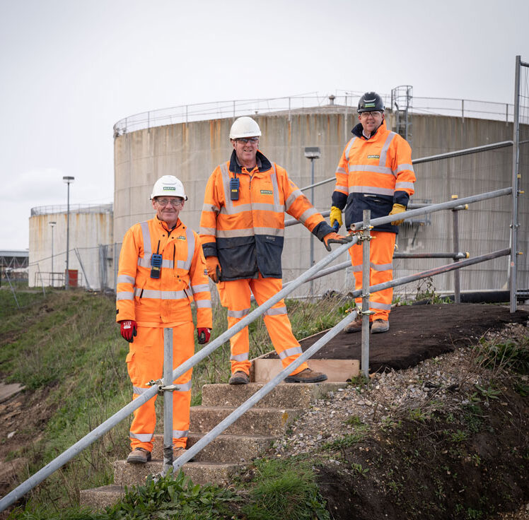 Three Murphy employees wearing orange high-visibility uniforms and safety helmets standing on some stairs at a construction site.