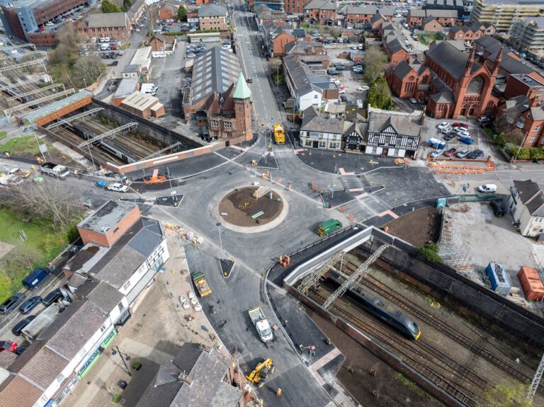 An aerial view of a roundabout on a bridge over train tracks in the day time.