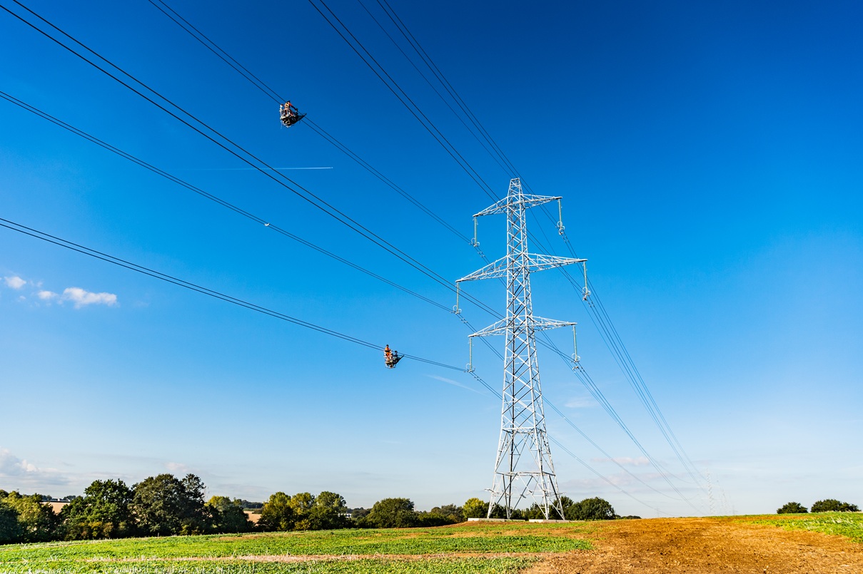 A pylon stands tall in an open field, with two Murphy workers performing maintenance to the transmission lines.